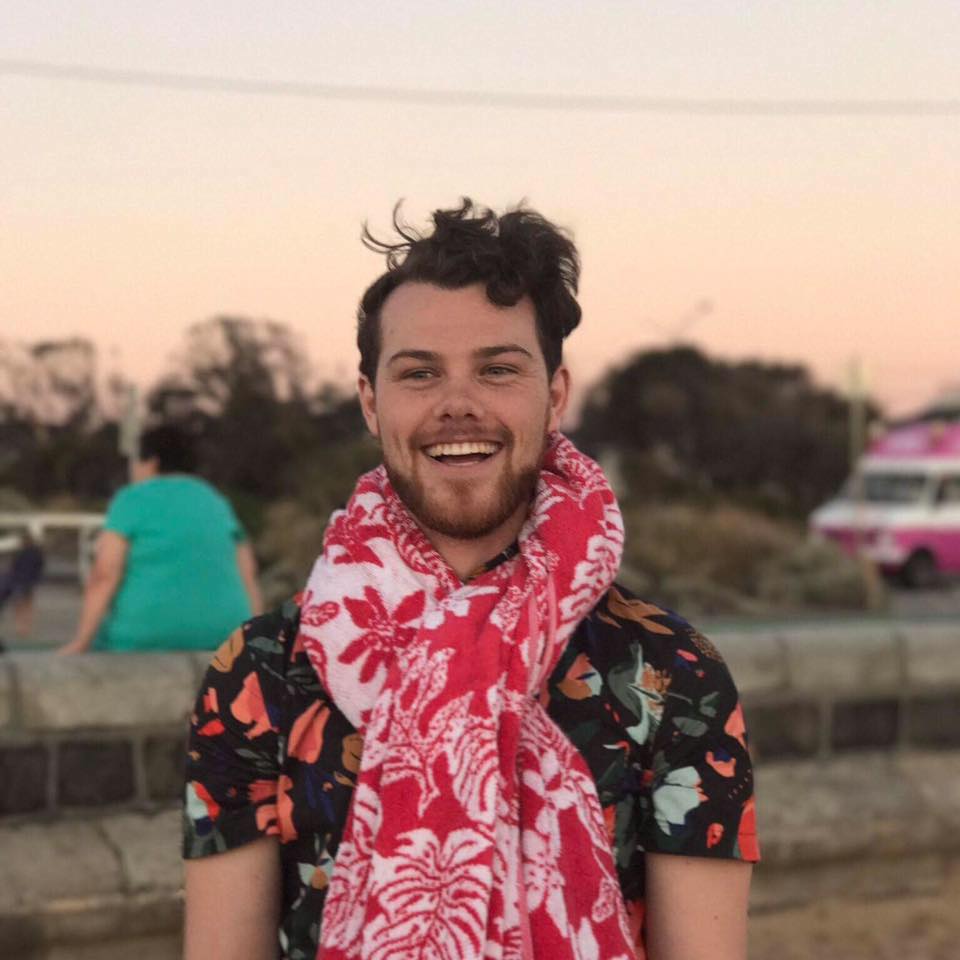 Tristan Marsh smiling in a red plaid shirt and tortoise shell glasses